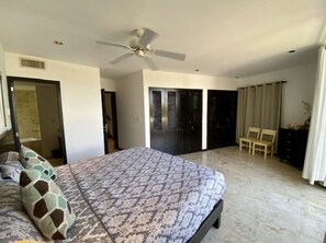 Een slaapkamer met een bed, een plafondventilator, een deur naar een balkon en een stoel.