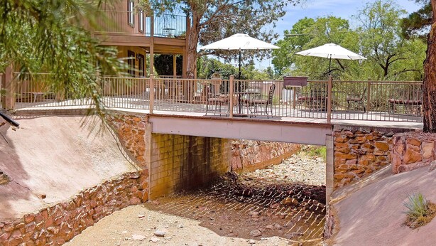 Un puente de piedra sobre un lecho de río seco, con mesas al aire libre y sombrillas.