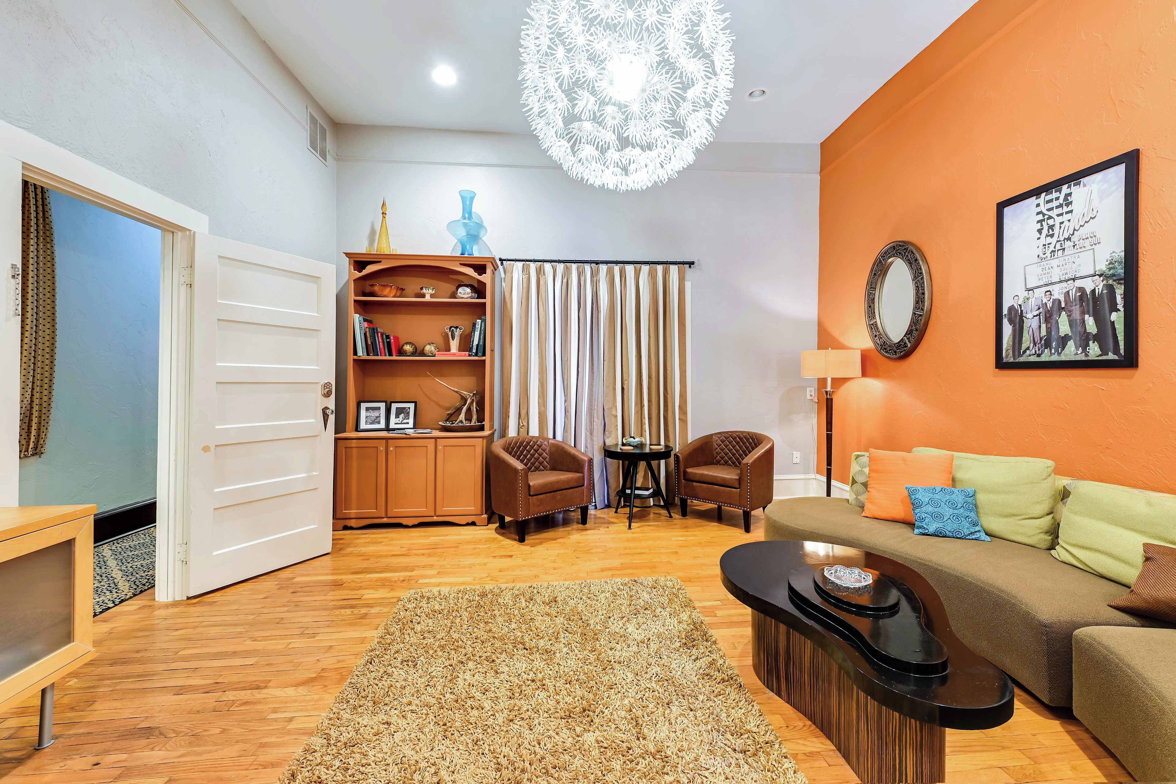 A living room with a sofa, chairs, a coffee table, a rug, a bookshelf, a mirror, and a chandelier.