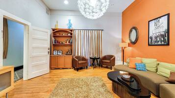 A living room with a sofa, chairs, a coffee table, a rug, a bookshelf, a mirror, and a chandelier.