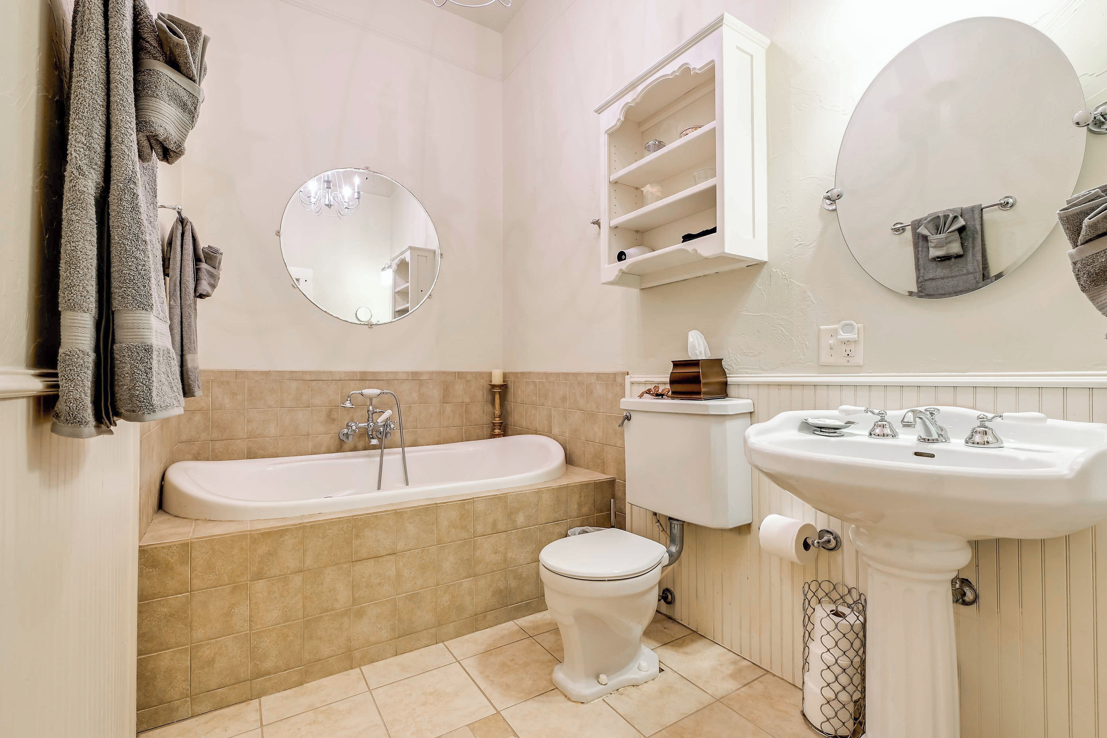Een badkamer met een bad, toilet, wastafel en twee spiegels.