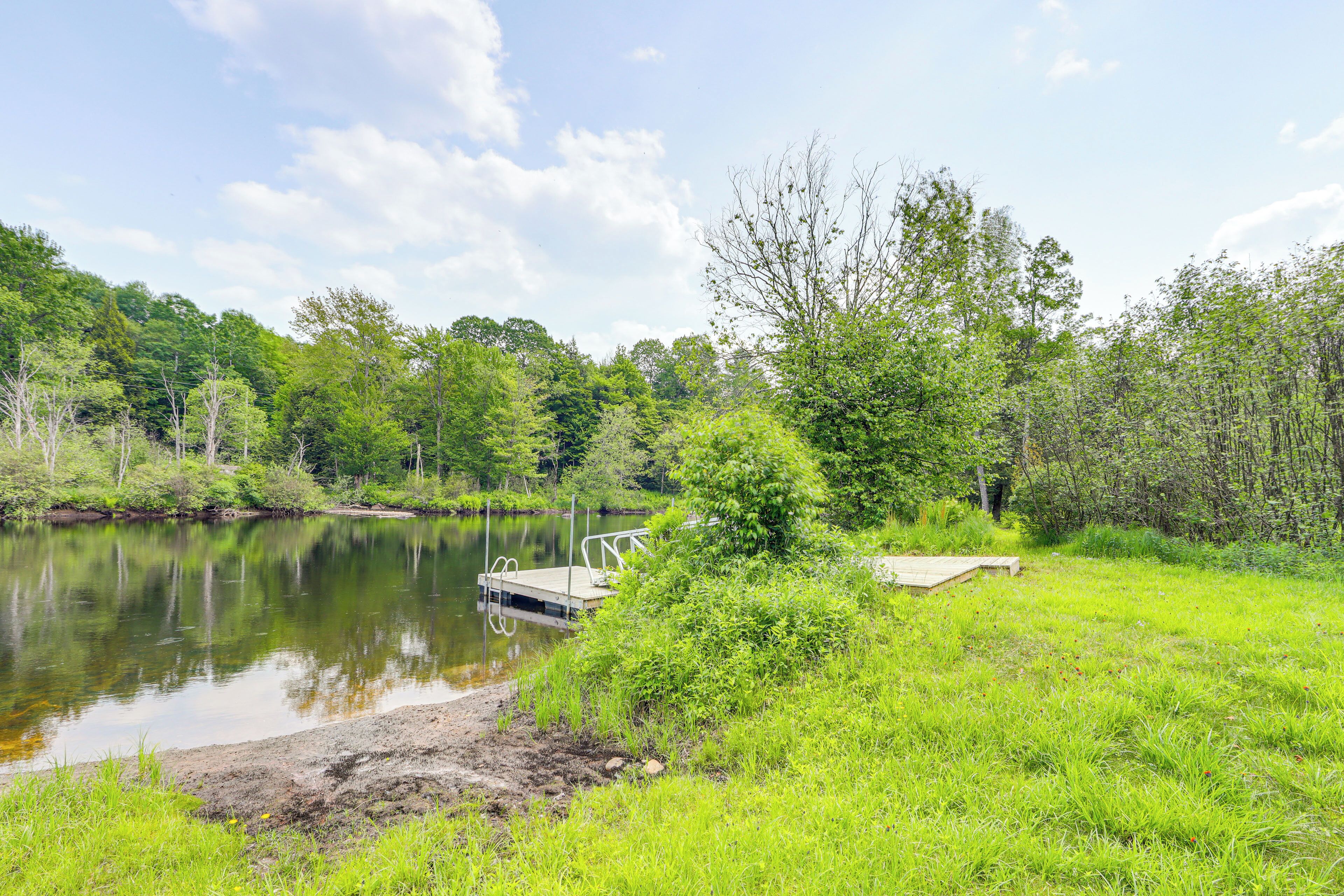 A serene lakeside scene with a dock extending into the water, surrounded by lush greenery and trees.