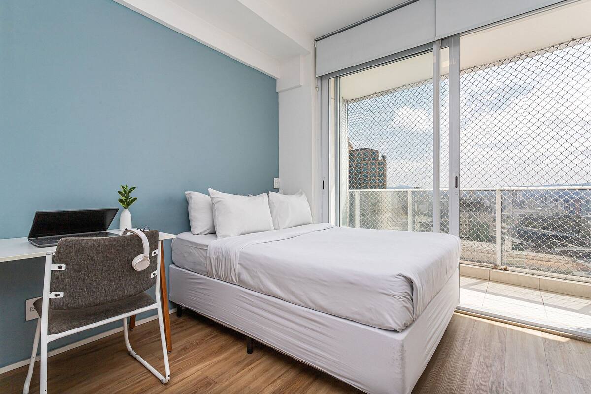 Une chambre à coucher avec un lit, un bureau avec un ordinateur portable et une chaise.