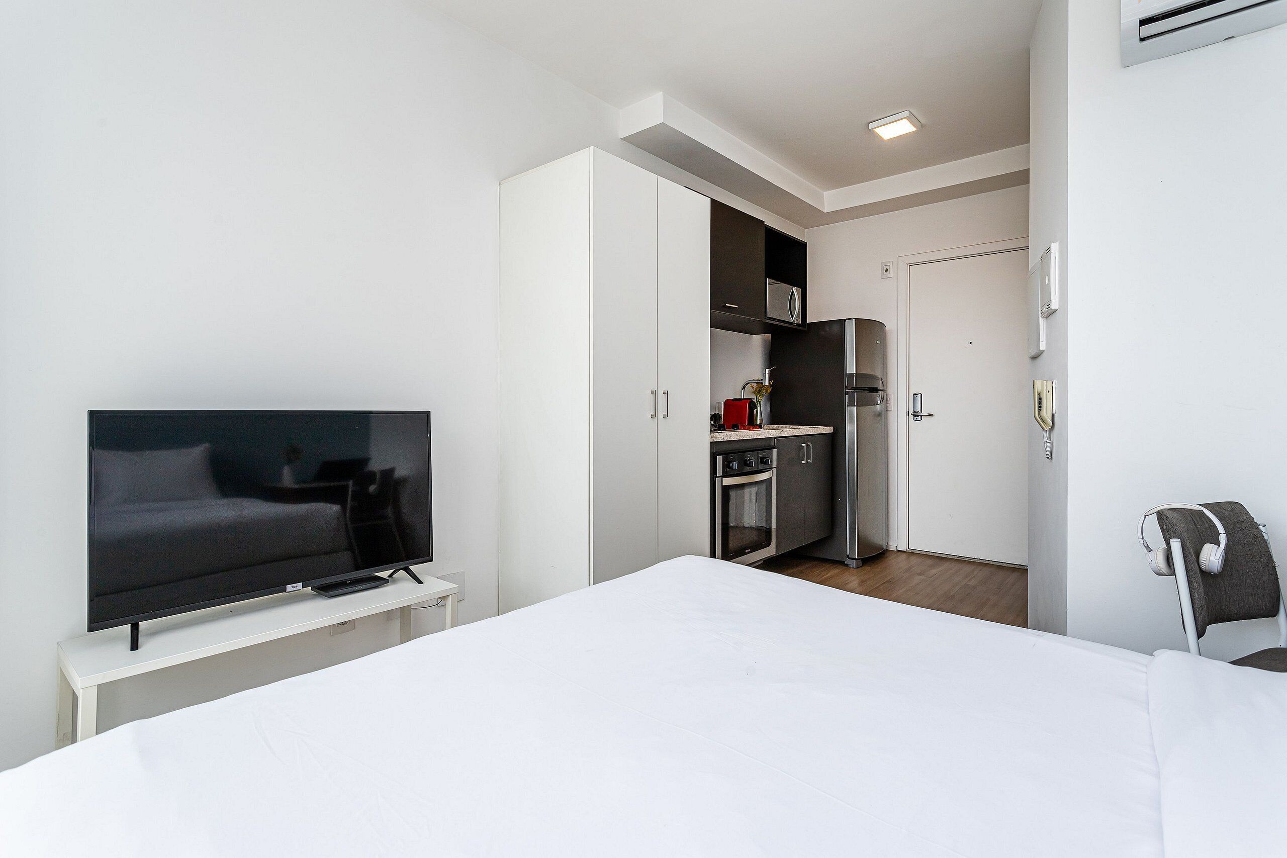 A modern hotel room with a large bed, a flat-screen TV, a kitchenette, and a small dining area.