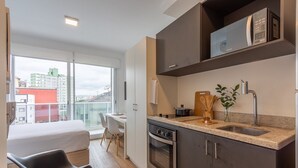 Una cocina moderna con horno integrado, microondas y lavabo. Hay una zona de comedor con mesa y sillas, y una cama con colchón blanco.