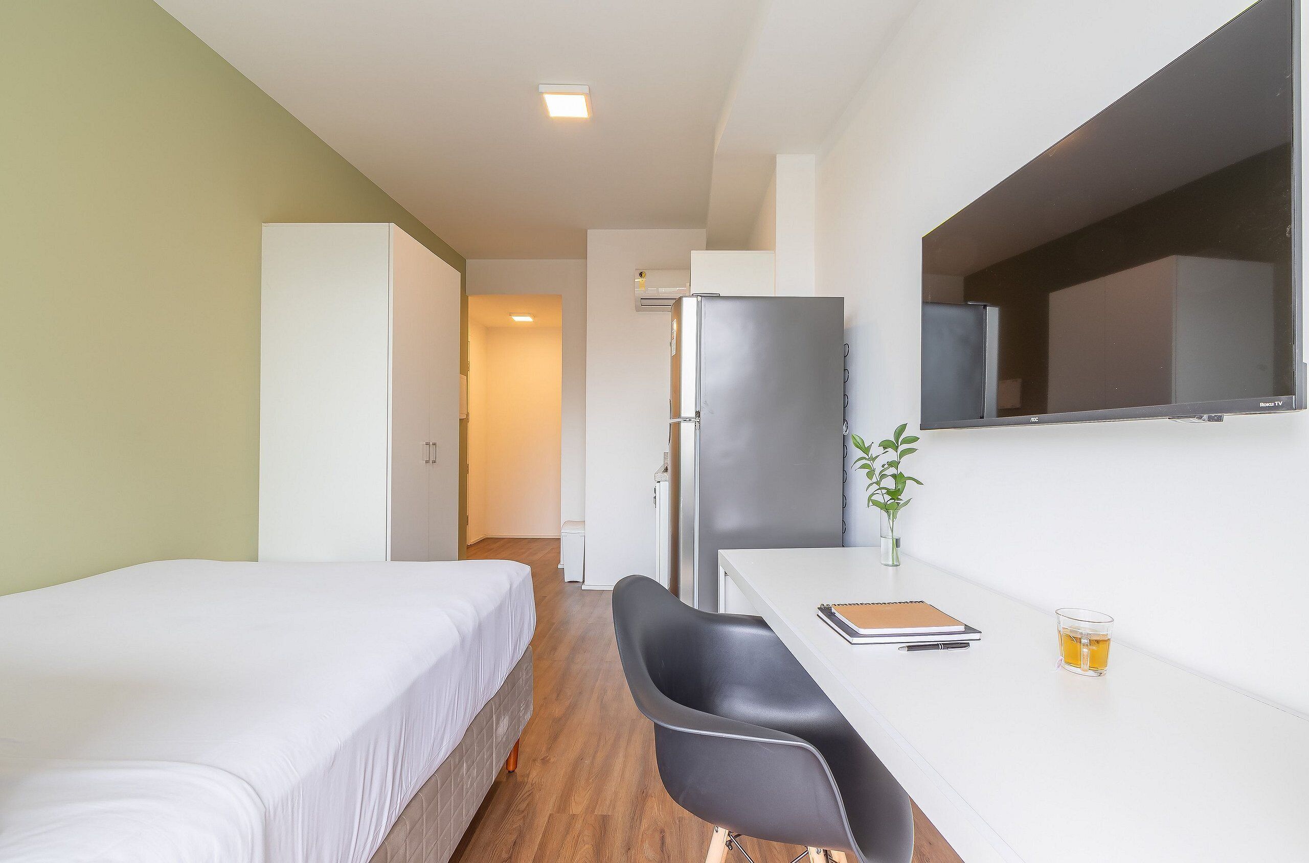 A hotel room with two single beds, a desk with a chair, a refrigerator, and a small plant.
