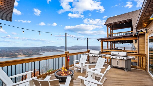 Terraza al aire libre con una chimenea, zona de parrillada y sillas Adirondack blancas.