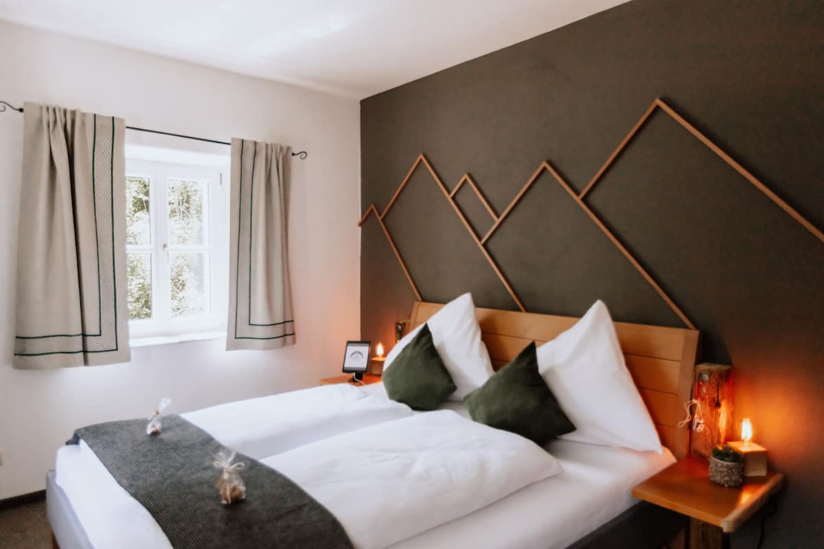 Une chambre d’hôtel avec un lit, des rideaux, une table de chevet et un luminaire fixé au mur.