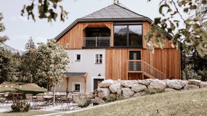 Une maison moderne à deux étages, dotée d’une façade en bois, d’un balcon et d’un mur en pierre à l’avant.