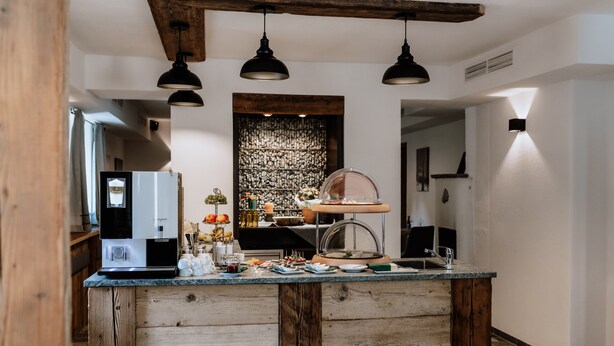 Une cuisine avec un îlot central en bois, des luminaires suspendus, une machine à café et un mur décoratif.