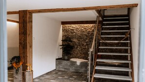 Un escalier avec une rampe en bois et des marches en métal, menant à un mur de pierre orné d’une plante et surmonté d’un tapis en fausse fourrure blanche.