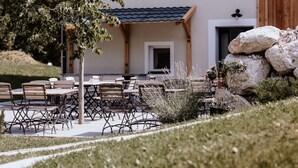 Une terrasse extérieure avec des tables et des chaises, une pergola en bois et un mur en pierre.