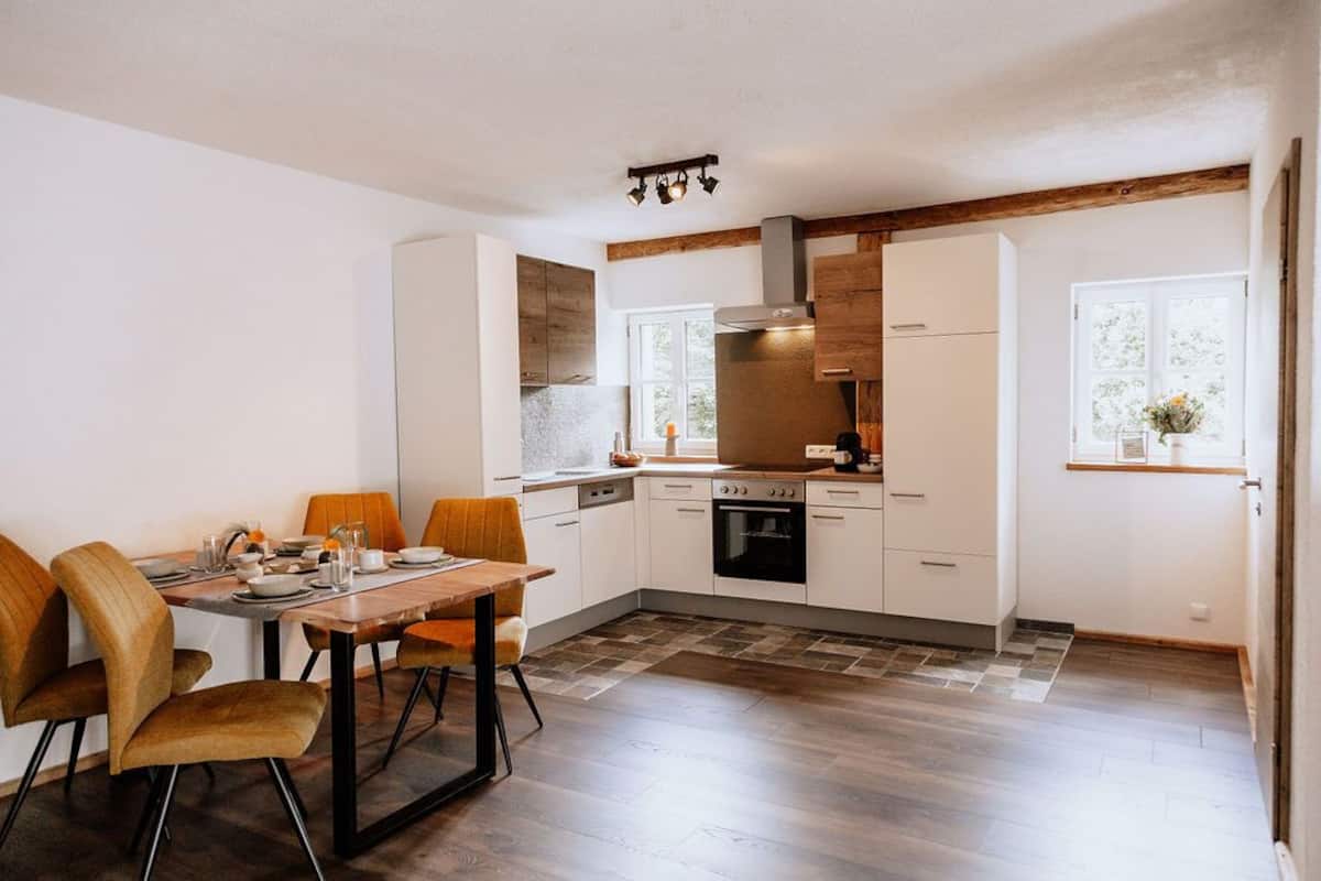 Une cuisine moderne avec des meubles blancs, une table à manger en bois et un four encastré.