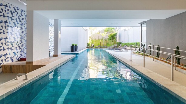 Een zwembad met helderblauw water, omgeven door een modern architectonisch ontwerp met witte muren en een geometrisch tegelpatroon aan één kant.