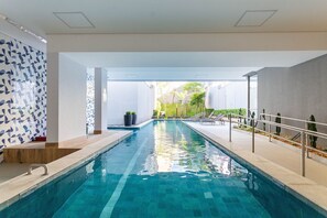 Une piscine à l’eau d’un bleu cristallin, entourée d’une architecture moderne caractérisée par des murs blancs et un motif géométrique en carreaux sur l’un des côtés.