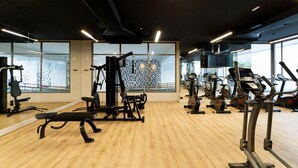 Een sportschool met trainingsapparatuur, grote ramen en een houten vloer.