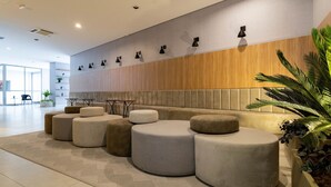 Een moderne lobby met een zithoek, voorzien van ronde poefs, een houten accentmuur en een potplant.