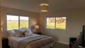 A bedroom with a large bed, two bedside tables, a desk with a chair, and two windows offering views of a field and trees. - NEW!  Charming Vineyard Cottage in the heart of the Russian river wine country! (Santa Rosa)
