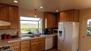 A modern kitchen with wooden cabinets, a white refrigerator, a gas stove, and a window providing a view of the outdoors. - NEW!  Charming Vineyard Cottage in the heart of the Russian river wine country! (Santa Rosa)
