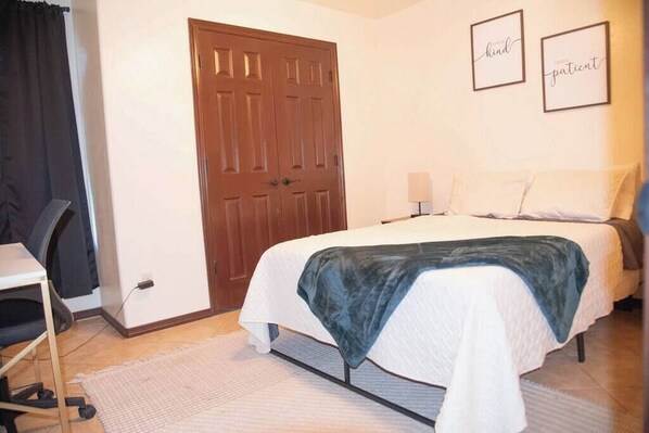 A bedroom with a bed, a desk, a chair, and a door.