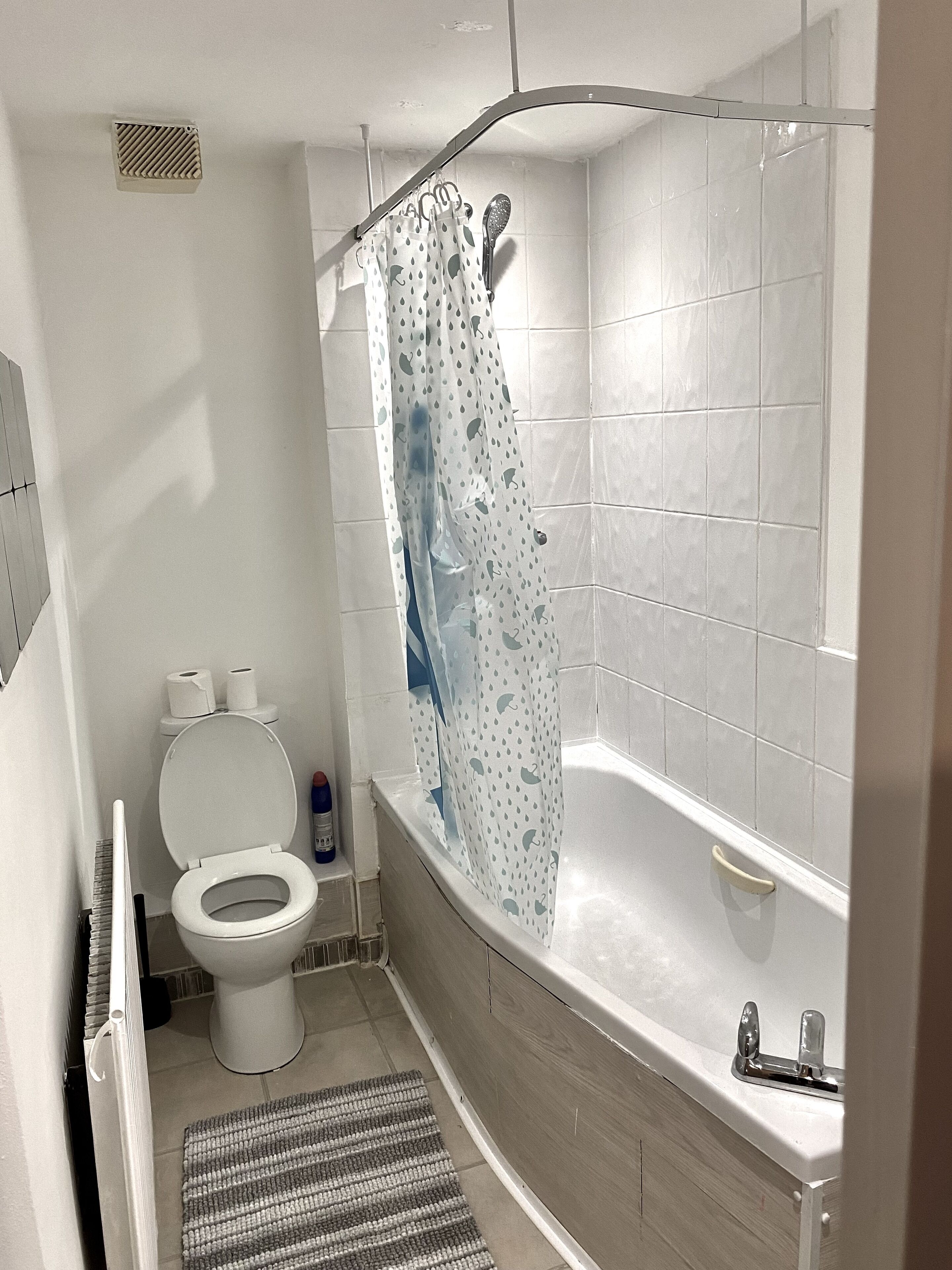 A bathroom with a toilet, a shower curtain, and a bathtub.