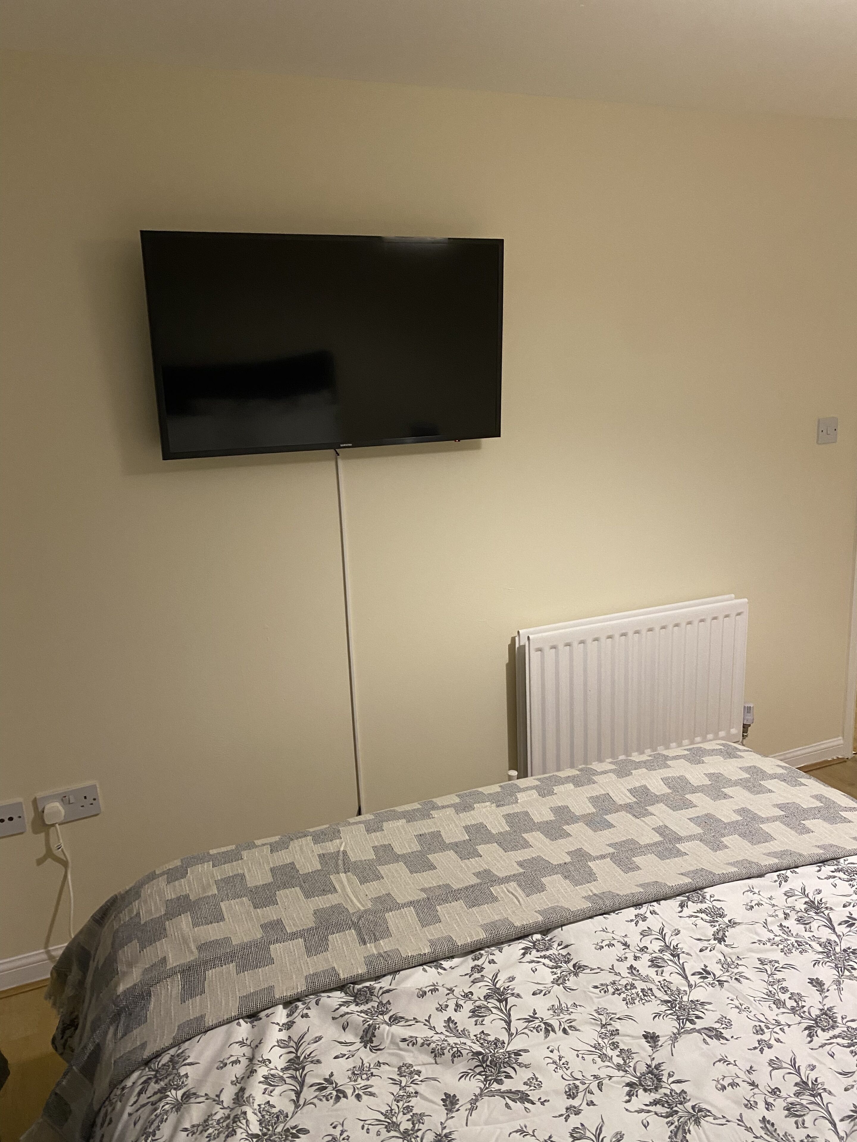 A bedroom with a bed, a wall-mounted TV, and a radiator.