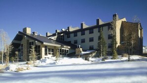 Un edificio de varios pisos con amplias ventanas y fachada de piedra, rodeado de nieve y árboles.