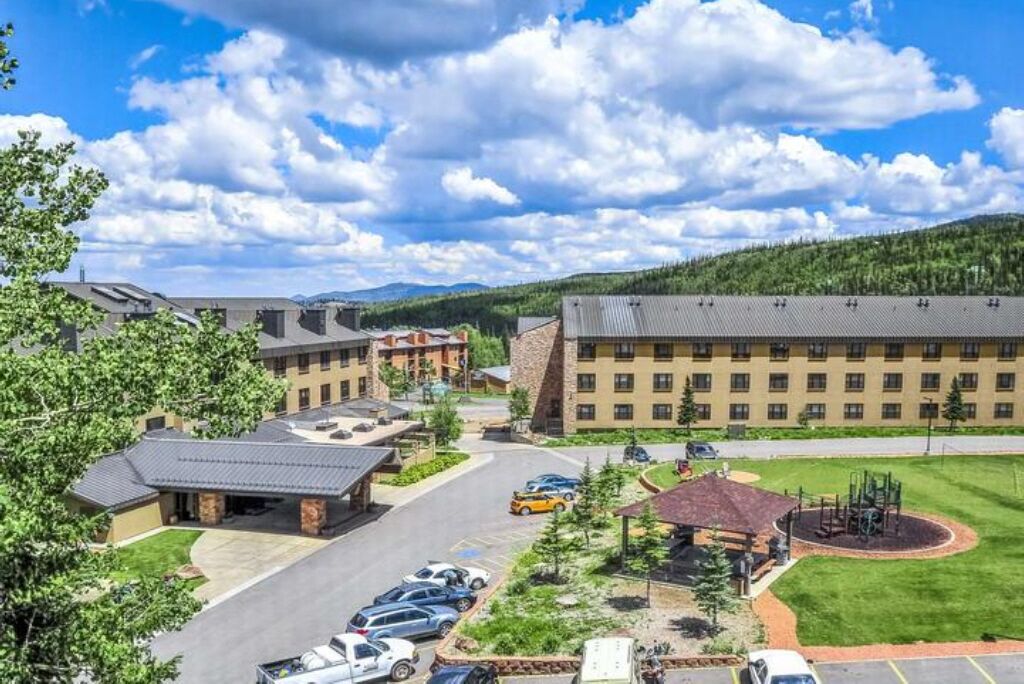 A hotel with a parking lot, a playground, and a mountain backdrop.