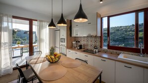 Een moderne keuken met een houten tafel, zwarte hanglampen en uitzicht op het landschap door grote ramen.
