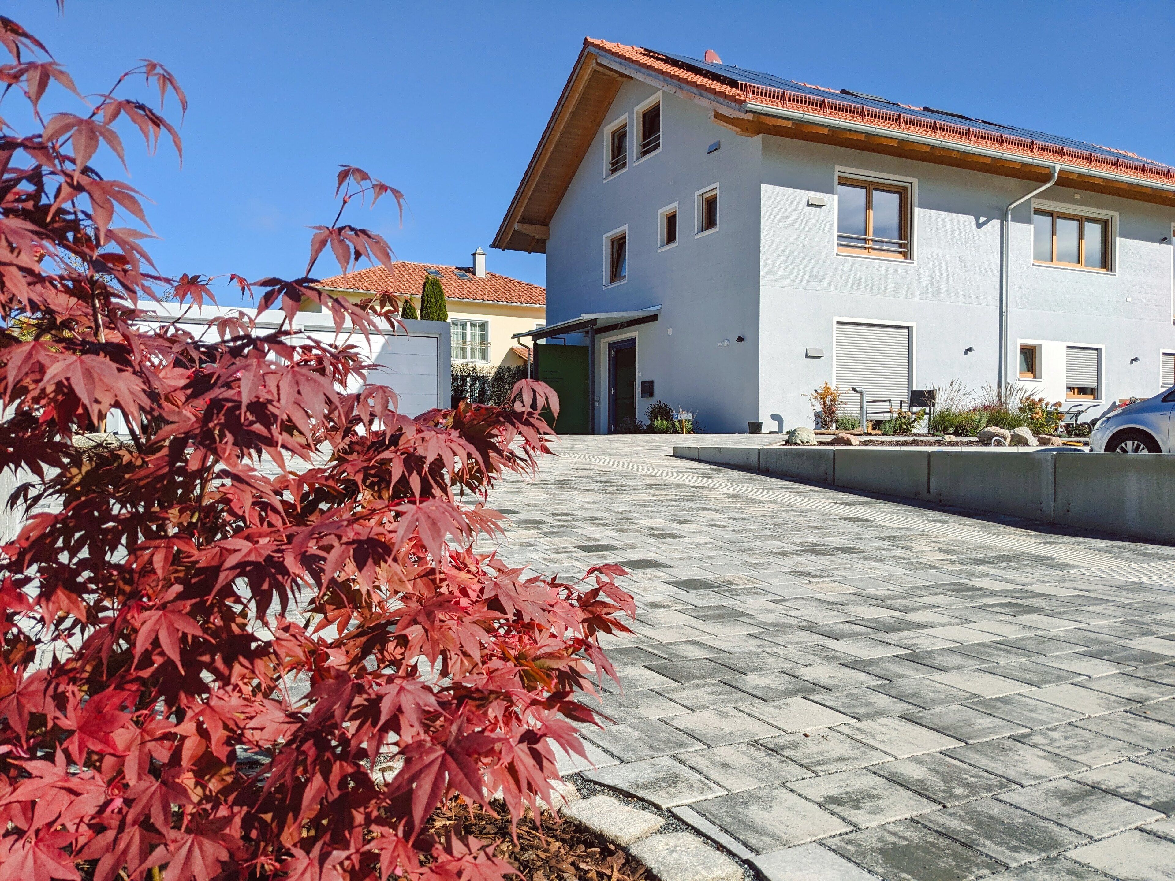 Ein modernes, zweistöckiges Haus mit Ziegeldach, einem gepflasterten Einfahrt und einem Garten mit Pflanzen mit roten Blättern.