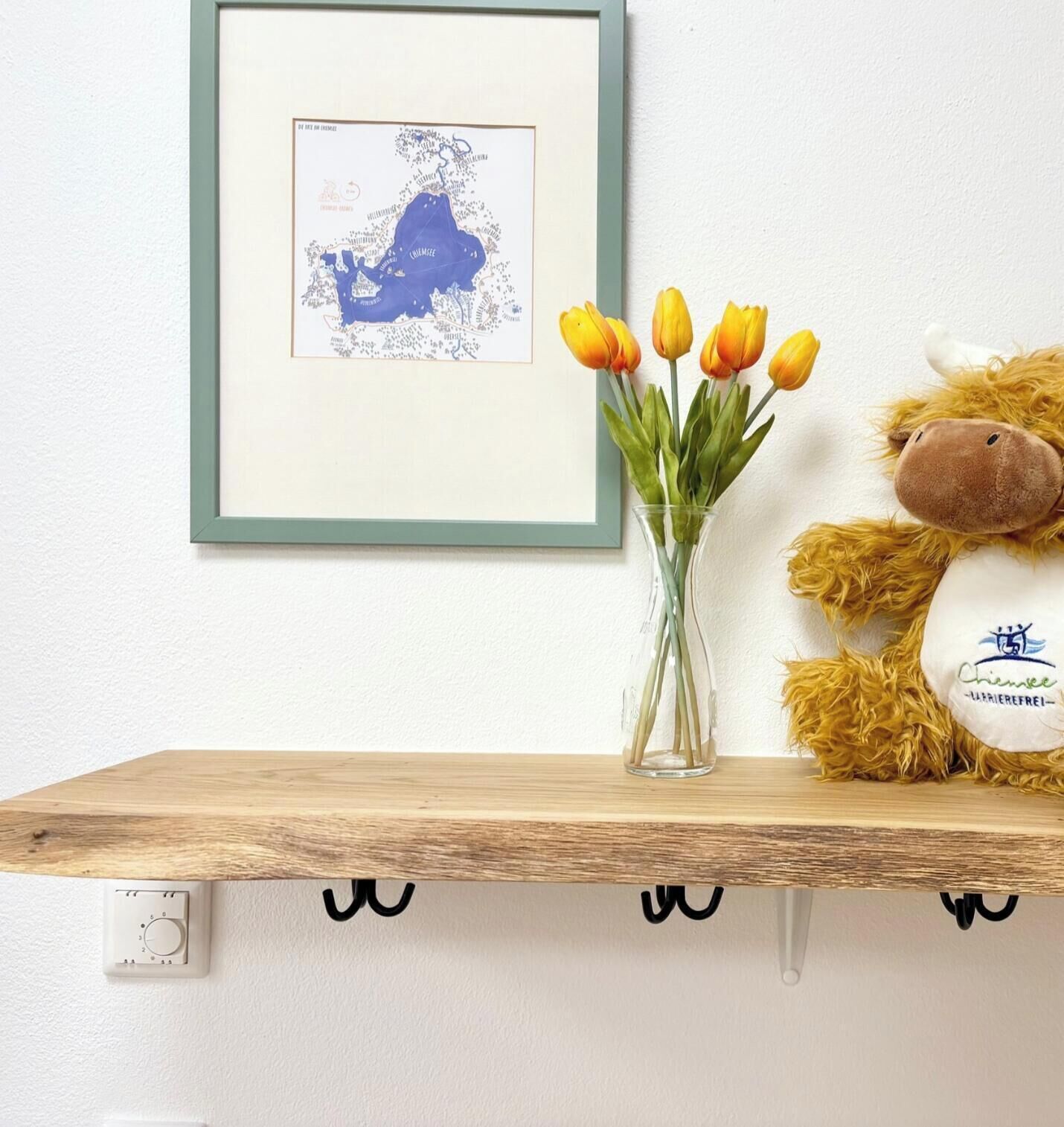 Eine gerahmte Karte an der Wand, eine Vase mit gelben Tulpen und ein Plüschtier auf einem Regal.