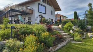 Une maison moderne à deux étages, dotée d’un jardin à l’avant, où l’on trouve une grande variété de plantes et de fleurs.