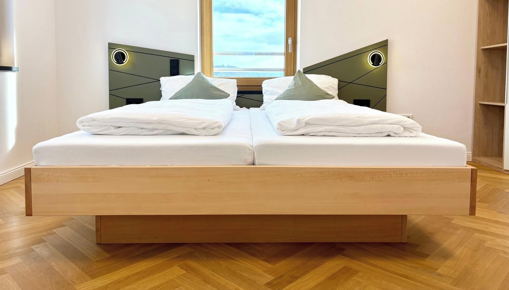 A double bed with a wooden frame, two bedside tables with illuminated panels, and a view of the sky through a window.