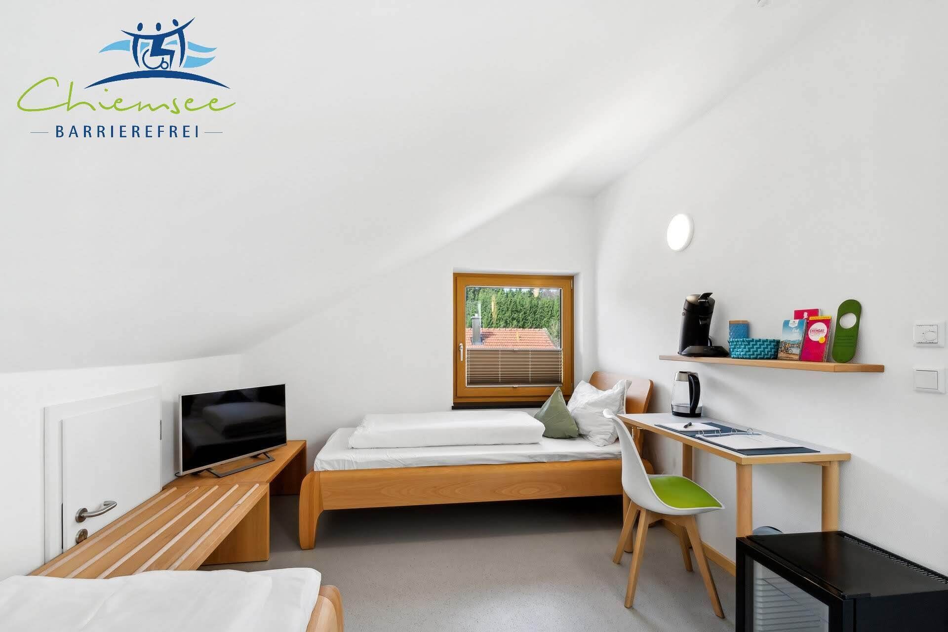 A small, modern room with a bed, a desk, a chair, a television, and a window with a view of trees.
