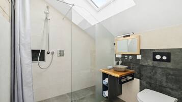 A modern bathroom with a skylight, a glass shower enclosure, a wooden vanity, and a white toilet.