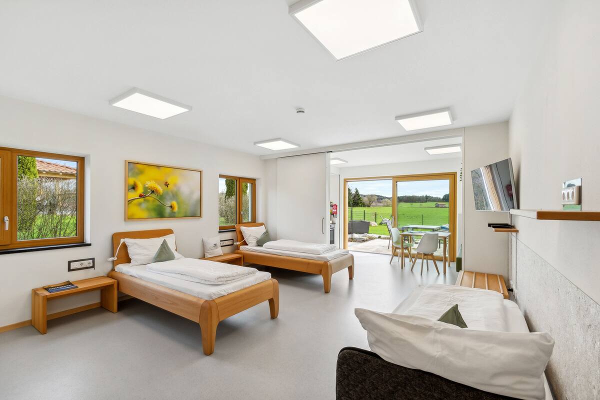A modern bedroom with two wooden beds, a desk, and a view of a garden.