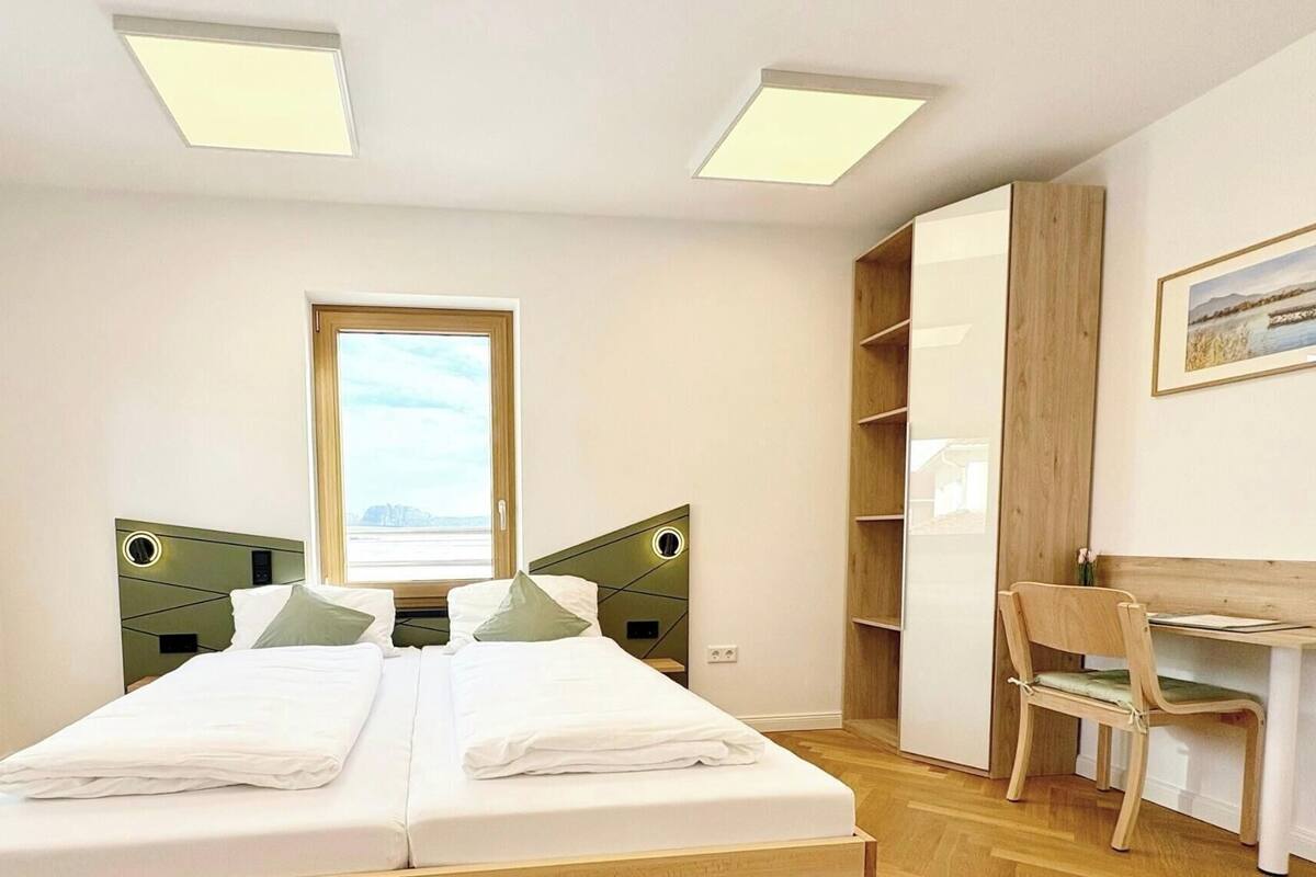 A double bed with a view of the city through a window, a desk with a chair, and a wardrobe.