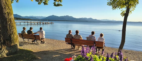 A group of people sitting on benches by a lake with mountains in the background.
