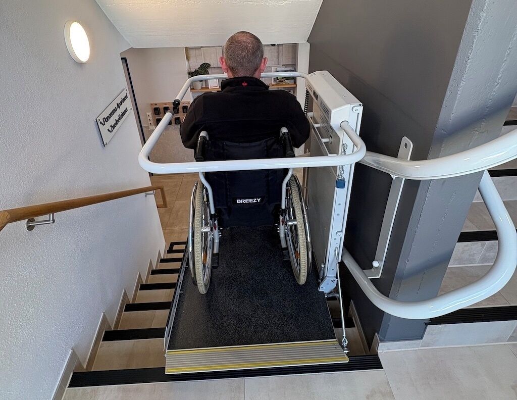 Une personne en fauteuil roulant utilise un monte-escalier pour monter un escalier.