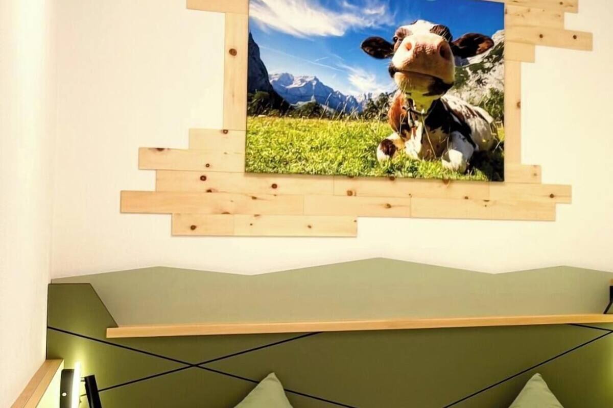 A bedroom with a bed, green pillows, a wooden headboard, and a wall-mounted picture of a cow in a field.