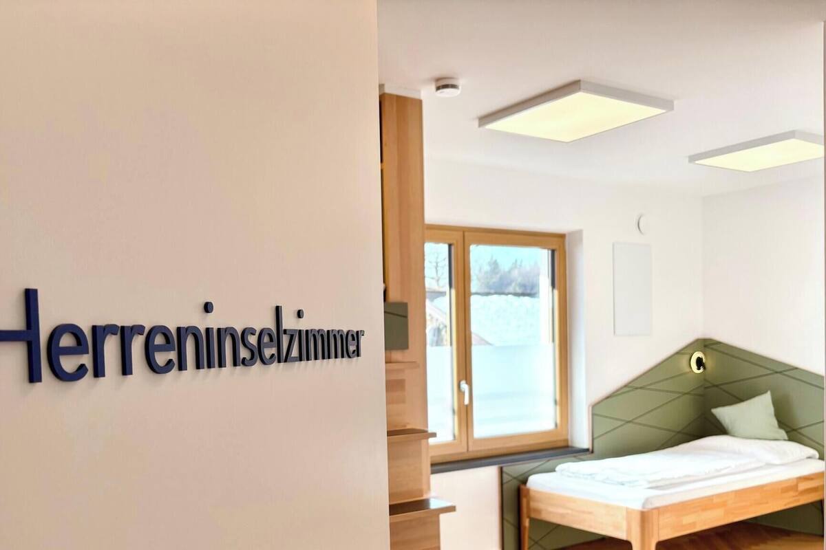 A hotel room with a bed, a window, and a sign reading "Herreninselzimmer".