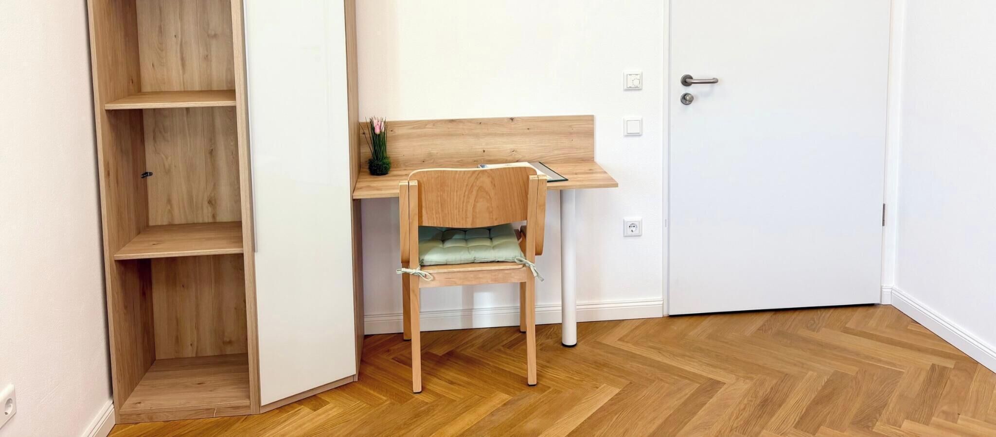 A room with a wooden desk, a chair, and a white door.