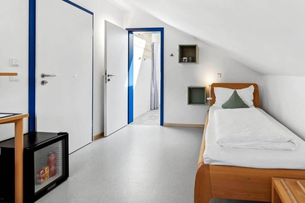A small, clean room with a single bed, a wooden nightstand, a small table, and a TV.