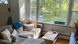 A living room with a sofa, ottoman, coffee table, and a large window with a view of trees.