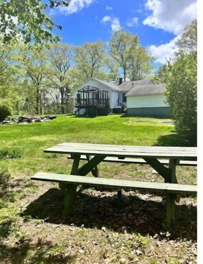 Ein Haus mit Veranda, umgeben von Bäumen und einem Picknicktisch im Vordergrund.