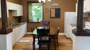A kitchen with white cabinets, a dining table with chairs, a chandelier, and a window with a view of greenery. - Williamsford Blacksmith Shop (Williamsford)