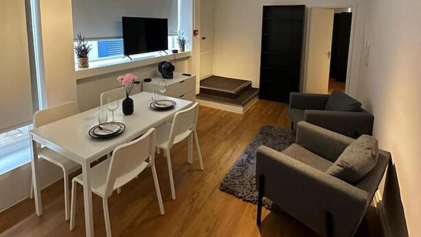 A modern living room with a dining area, a flat-screen TV mounted on the wall, a grey sofa, and a small rug. - Charming Studio in Bond Street (London)