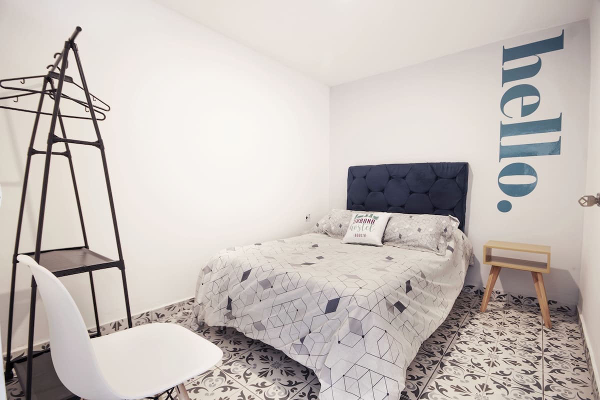 Un dormitorio con una cama, una silla blanca, un estante de metal negro y una pared con la palabra 'hello' escrita en letras grandes.