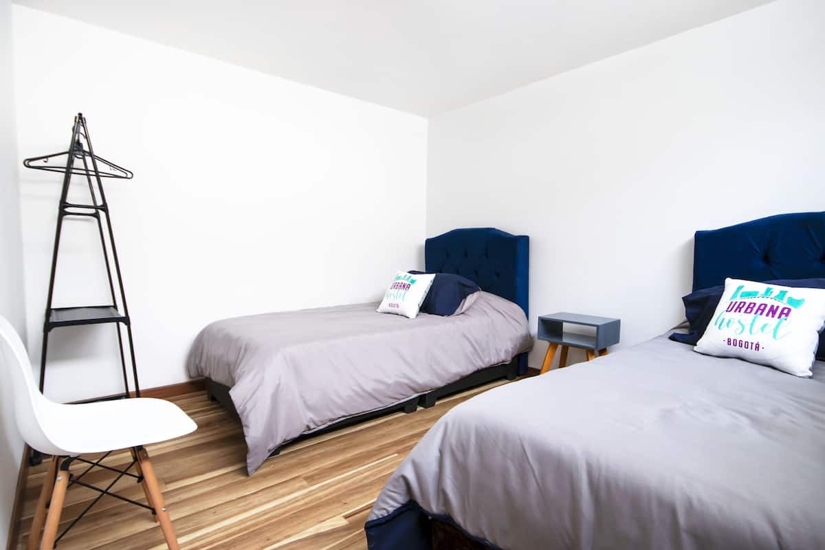 Una habitación con dos camas individuales, una silla, una mesita y una escalera.