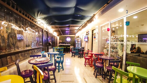 A restaurant with colorful tables and chairs, a bar area, and a view of the street. - Urbana Hostel (Bogotá)